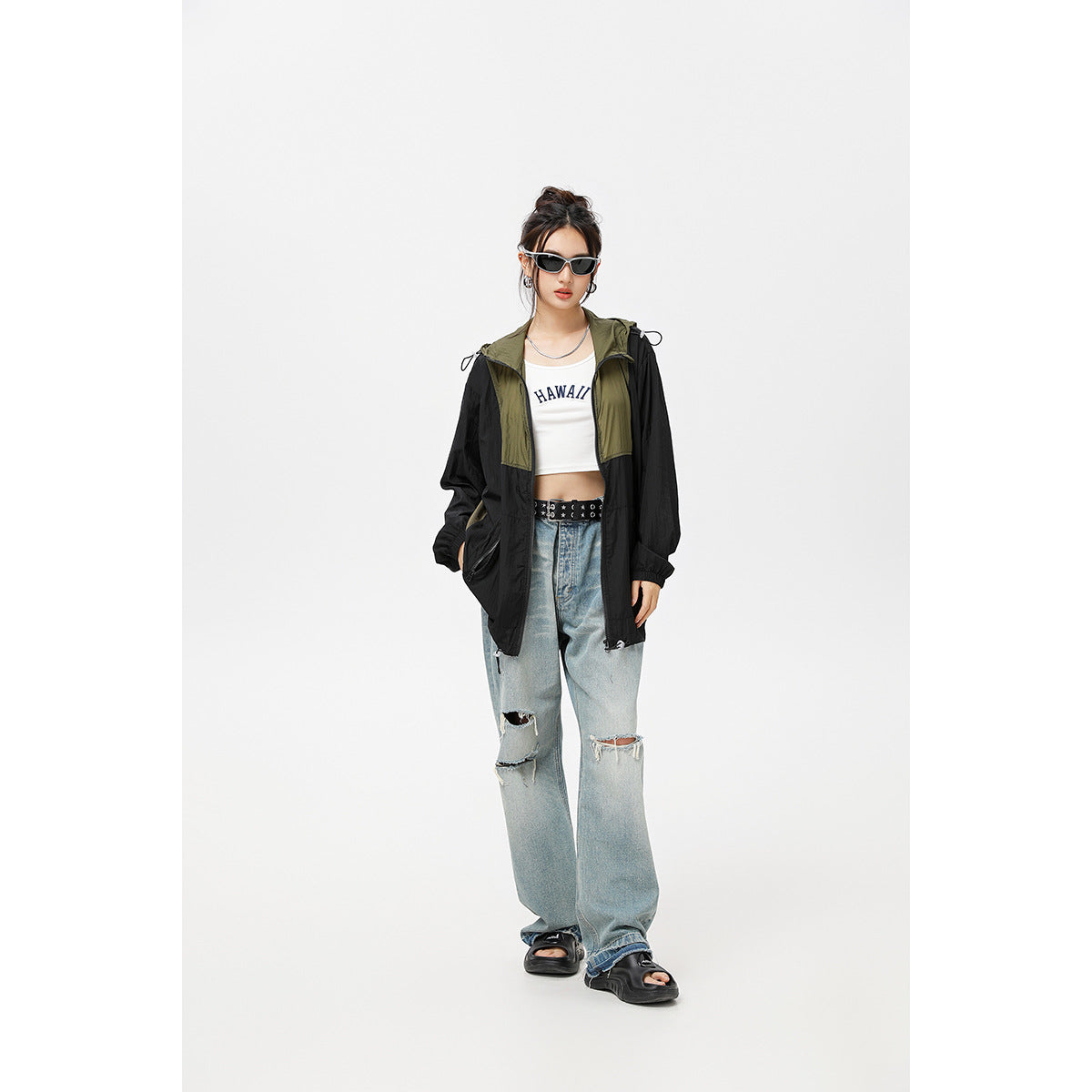 Model wearing a black and olive hooded windbreaker over a white crop top with loose distressed jeans.