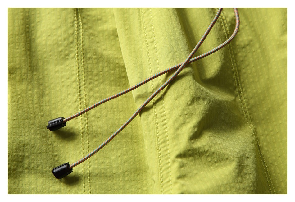 Close-up of yellow-green pants with multicolored drawcords and black toggles against the textured fabric.