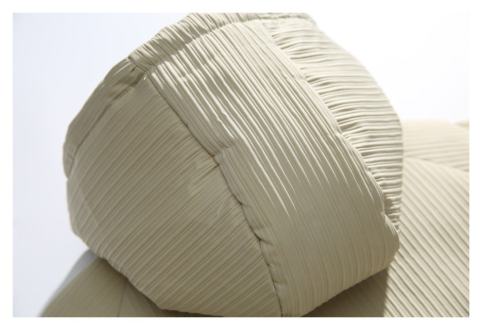 Close-up of curved stitched panels and fine pleating on an ivory garment.