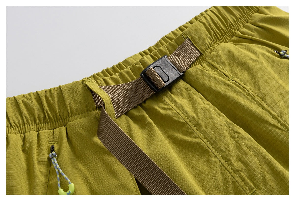 Close-up of olive-yellow shorts with an elastic waistband, brown webbing belt and black buckle.