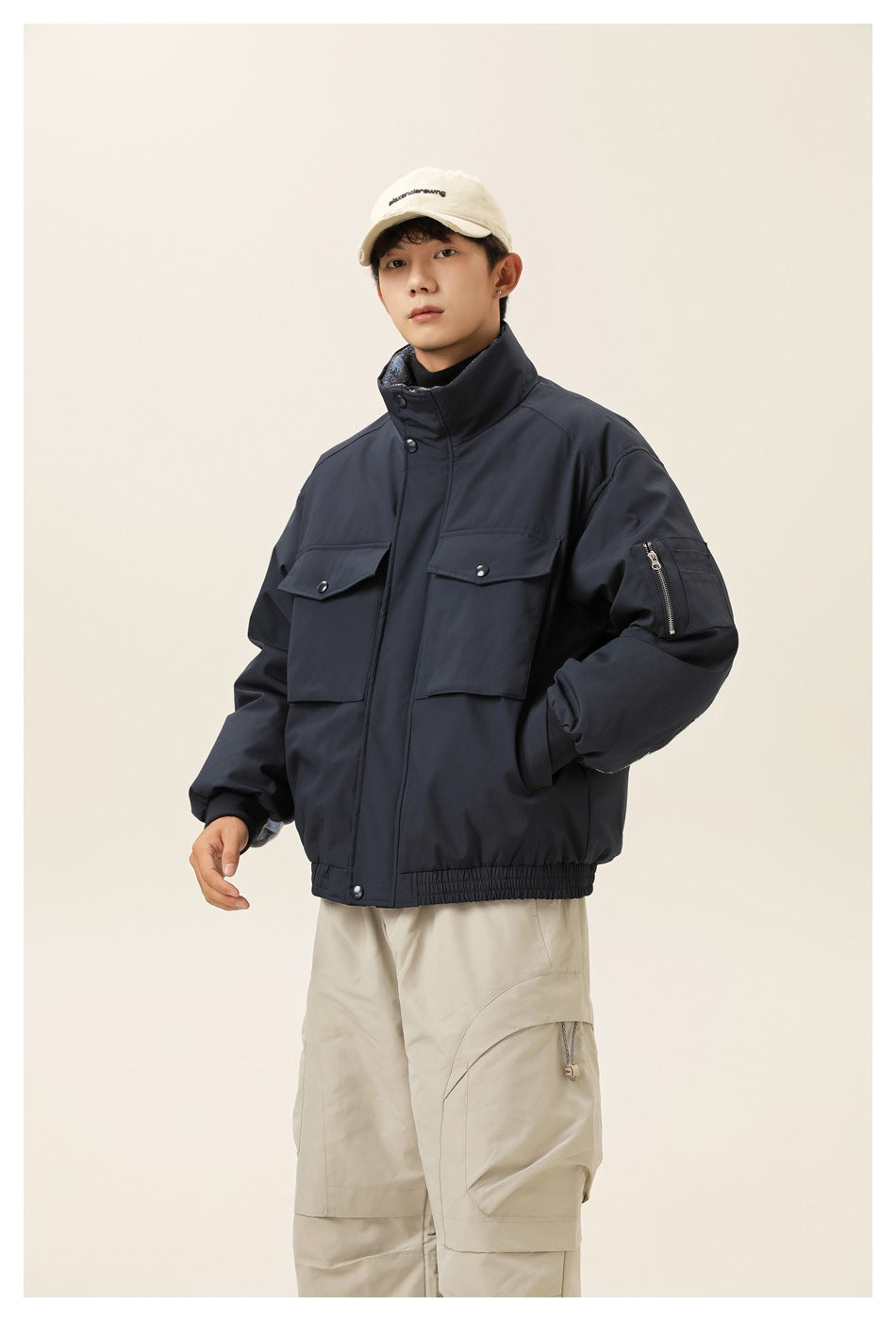 Model wearing a navy utility jacket with a high collar, two flap chest pockets, a zippered sleeve pocket and gathered hem.