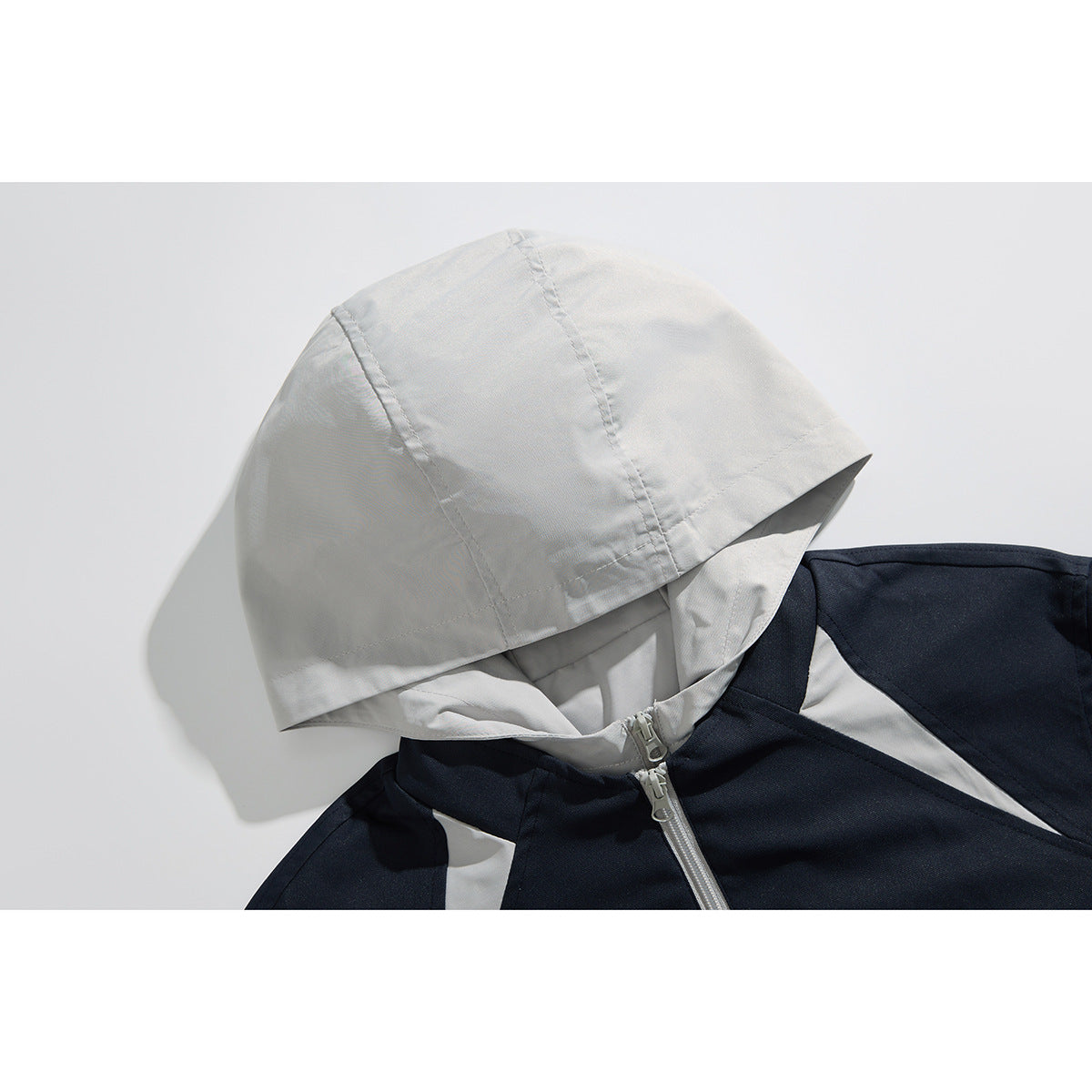Close-up of a navy hooded jacket with a light gray hood, shoulder panels, and front zipper.
