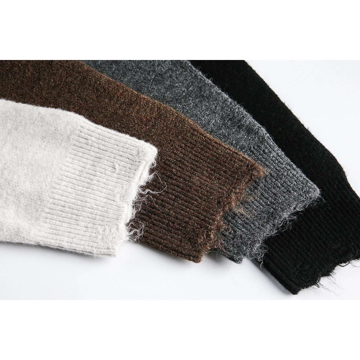 Close-up of sweater sleeve cuffs in ivory, brown, charcoal gray, and black, with ribbed knit and loose fibers.