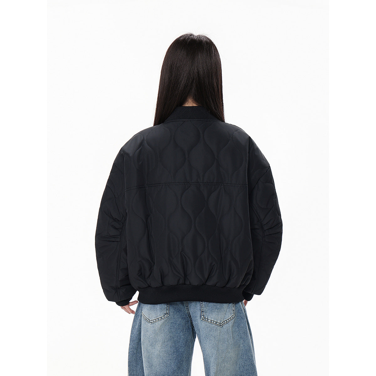 Back view of a model wearing a black quilted bomber jacket with ribbed collar and hem.