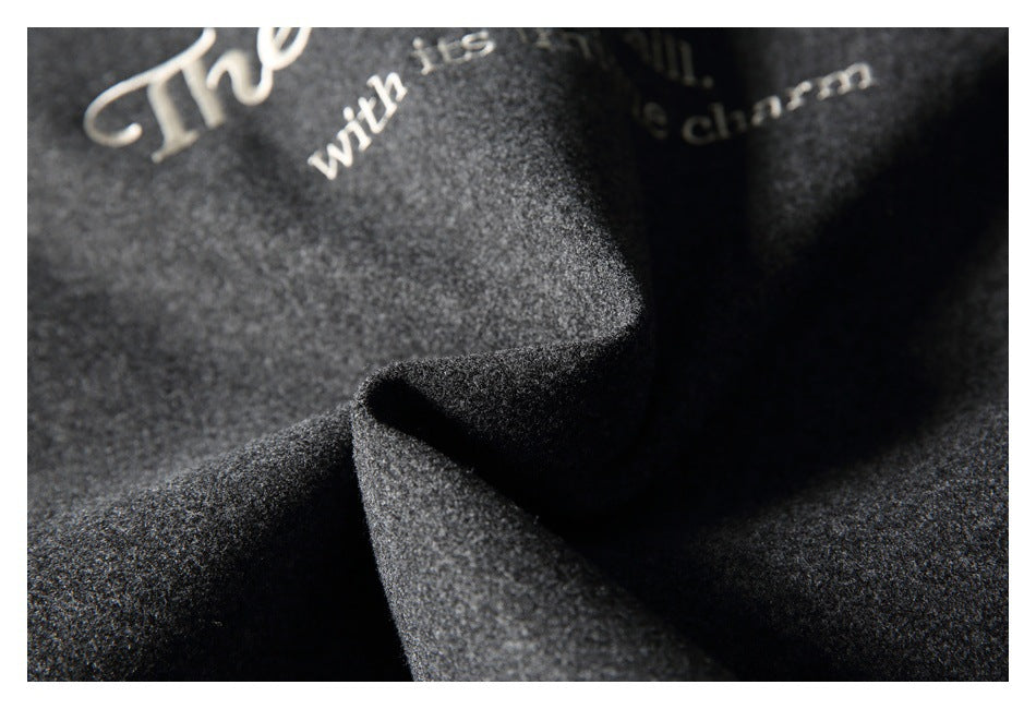 Close-up of charcoal gray coat fabric in soft folds, with partial cream embroidery visible.