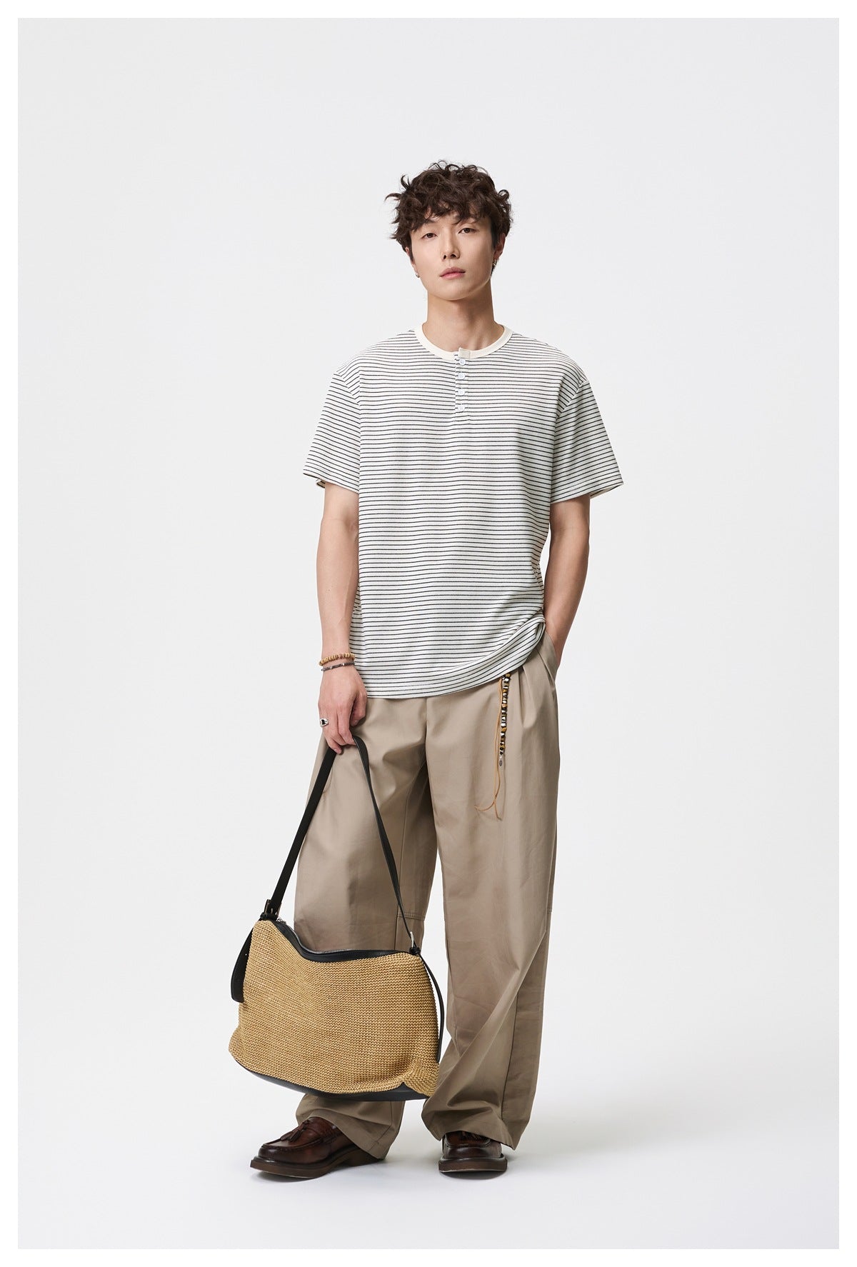 Model wearing an ivory T-shirt with thin black stripes, a short button placket, and beige trousers.