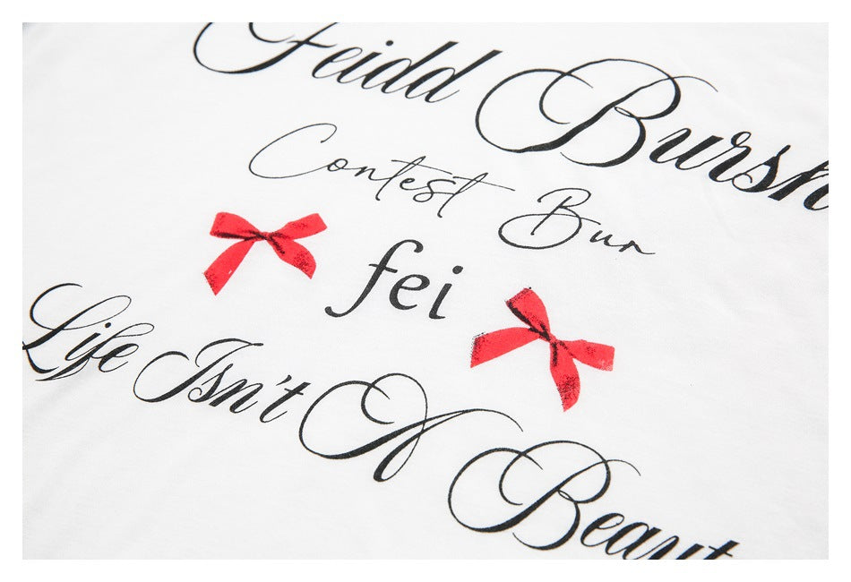 Close-up of black cursive lettering and two red bow prints on white shirt fabric.
