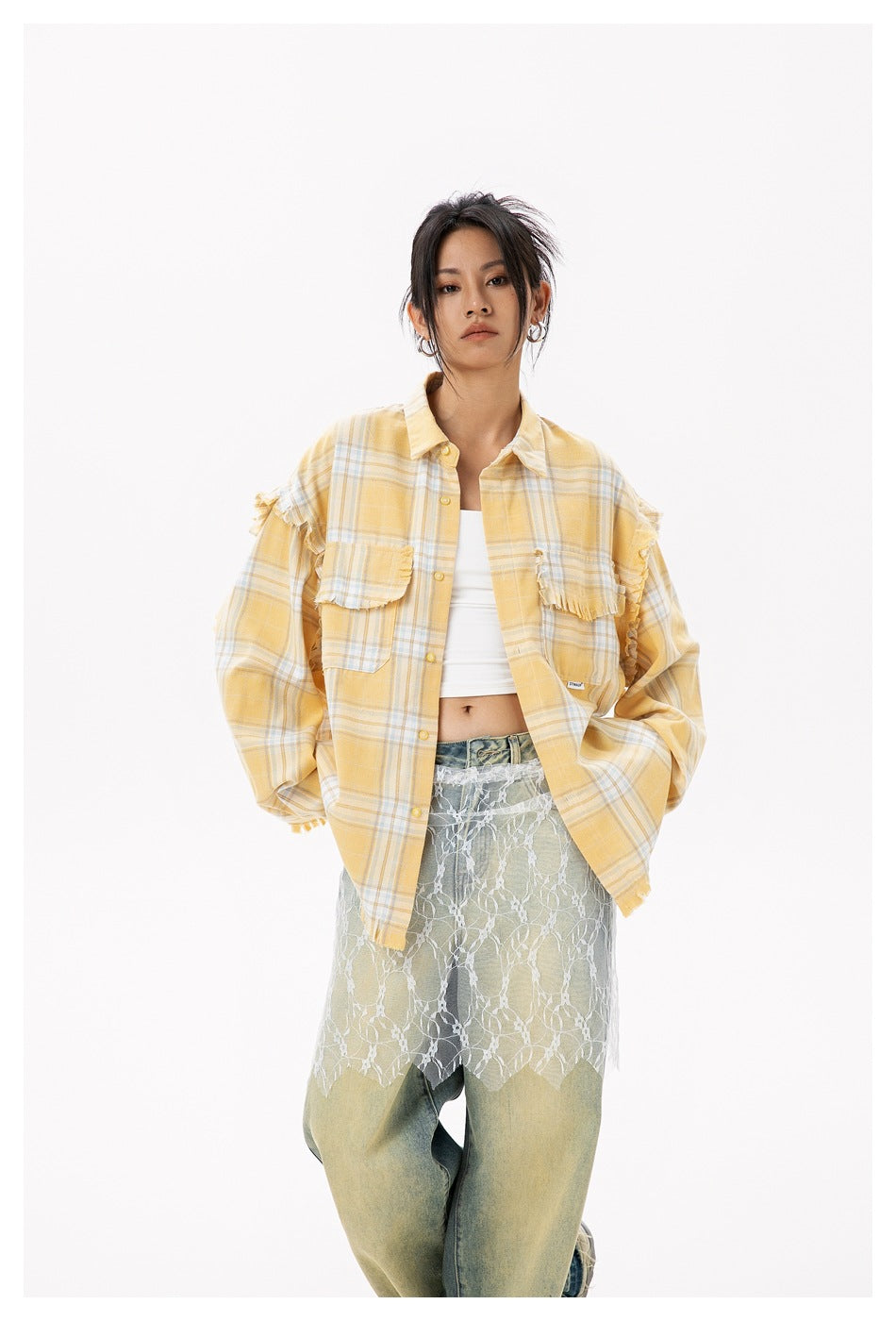 Front view of a model wearing an oversized yellow plaid button-up with frayed details and chest pockets, over a white top and