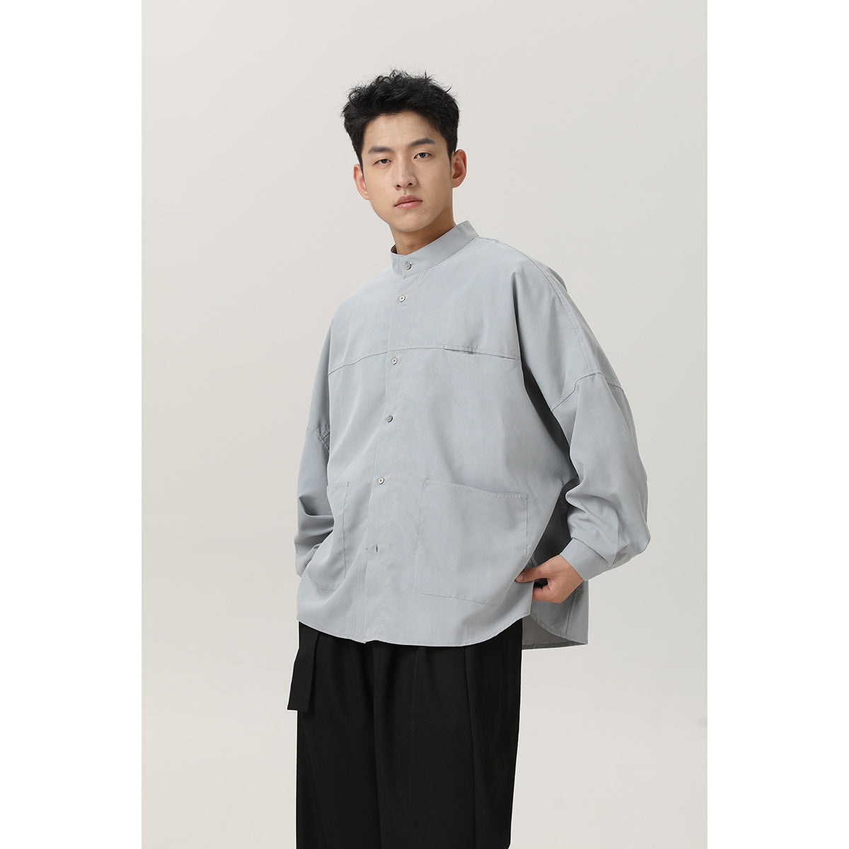 Model wearing a light gray oversized stand-collar shirt with button front, dropped sleeves, and two front patch pockets.