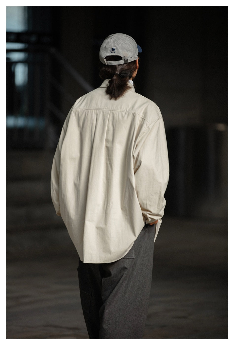Back view of a model wearing a loose cream button-up shirt with dark trousers.
