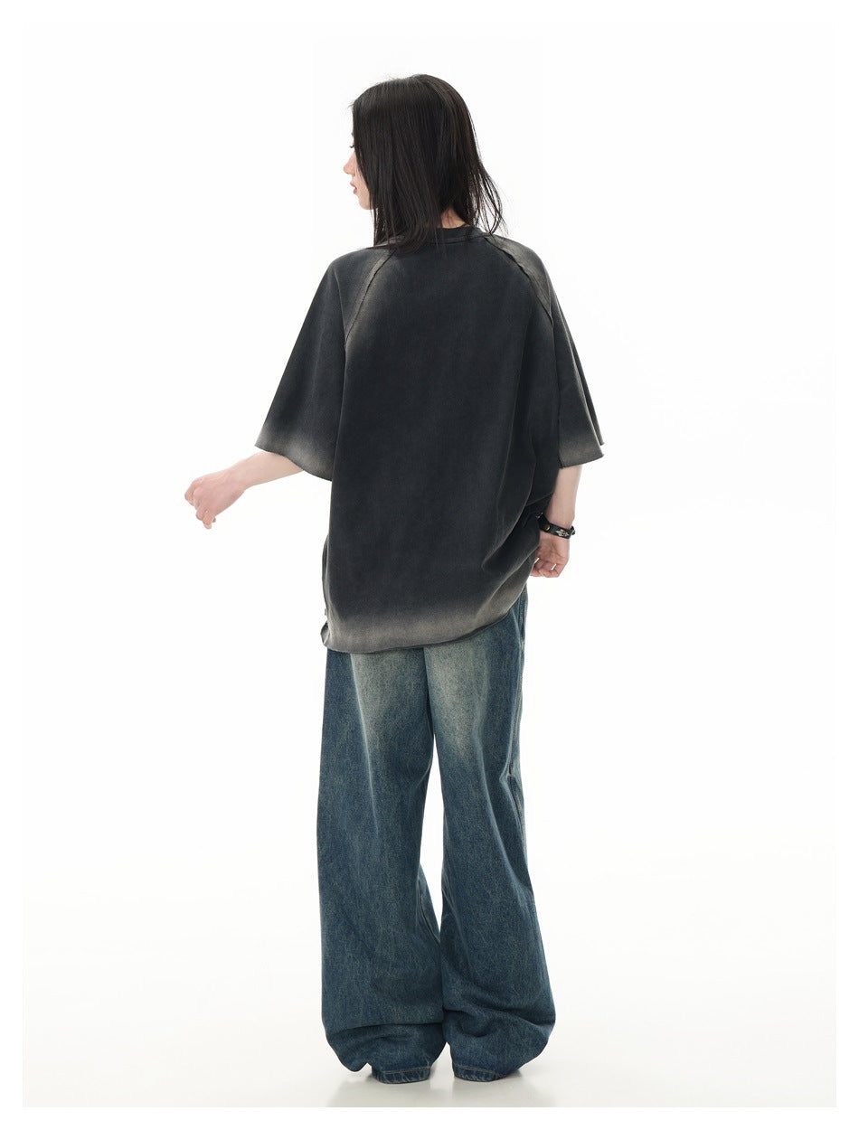 Rear view of a model wearing an oversized charcoal T-shirt with faded gray accents and raglan seams.