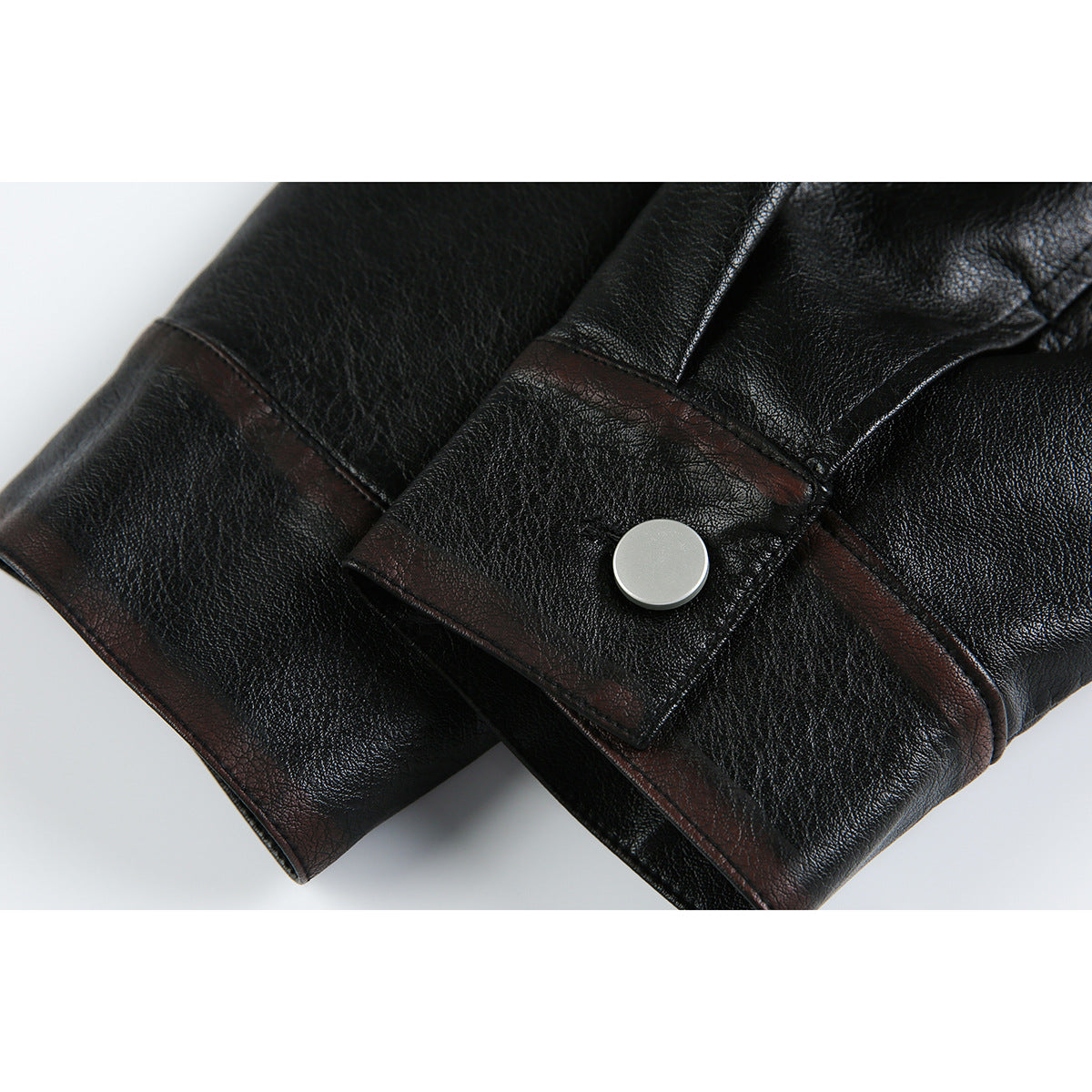 Close-up of a black jacket sleeve cuff with dark brown trim and a silver snap button.