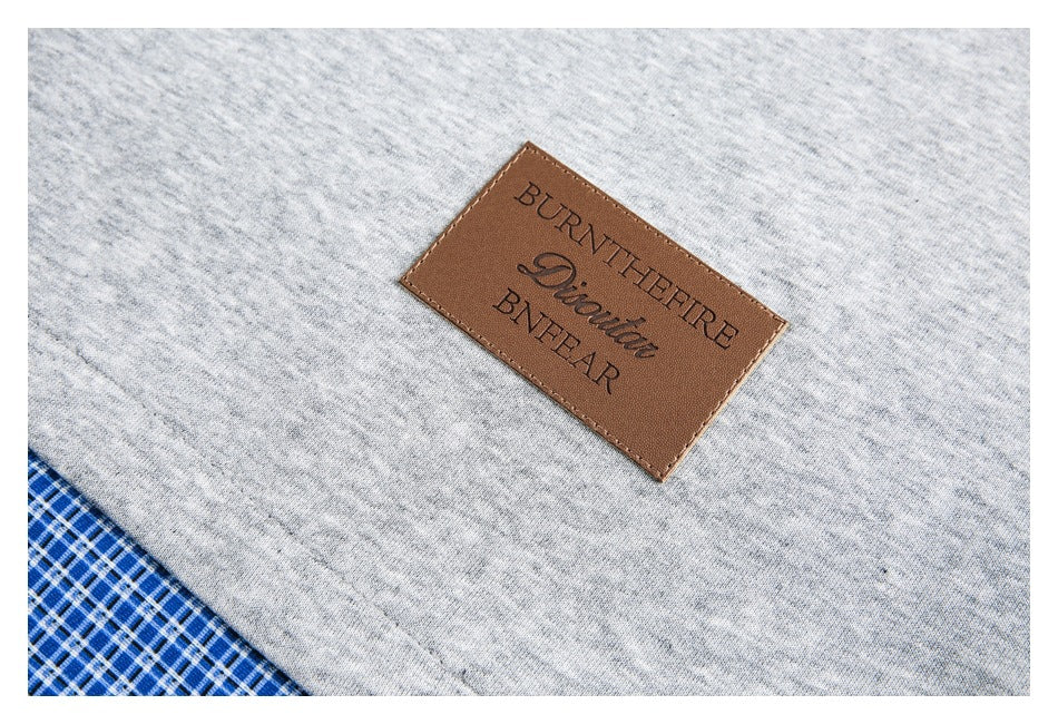 Close-up of a brown brand label on heather gray fabric, with blue-and-white plaid fabric at the corner.