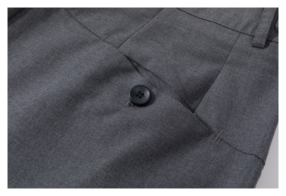 Close-up of a black button and pleated waistband on charcoal gray trousers.