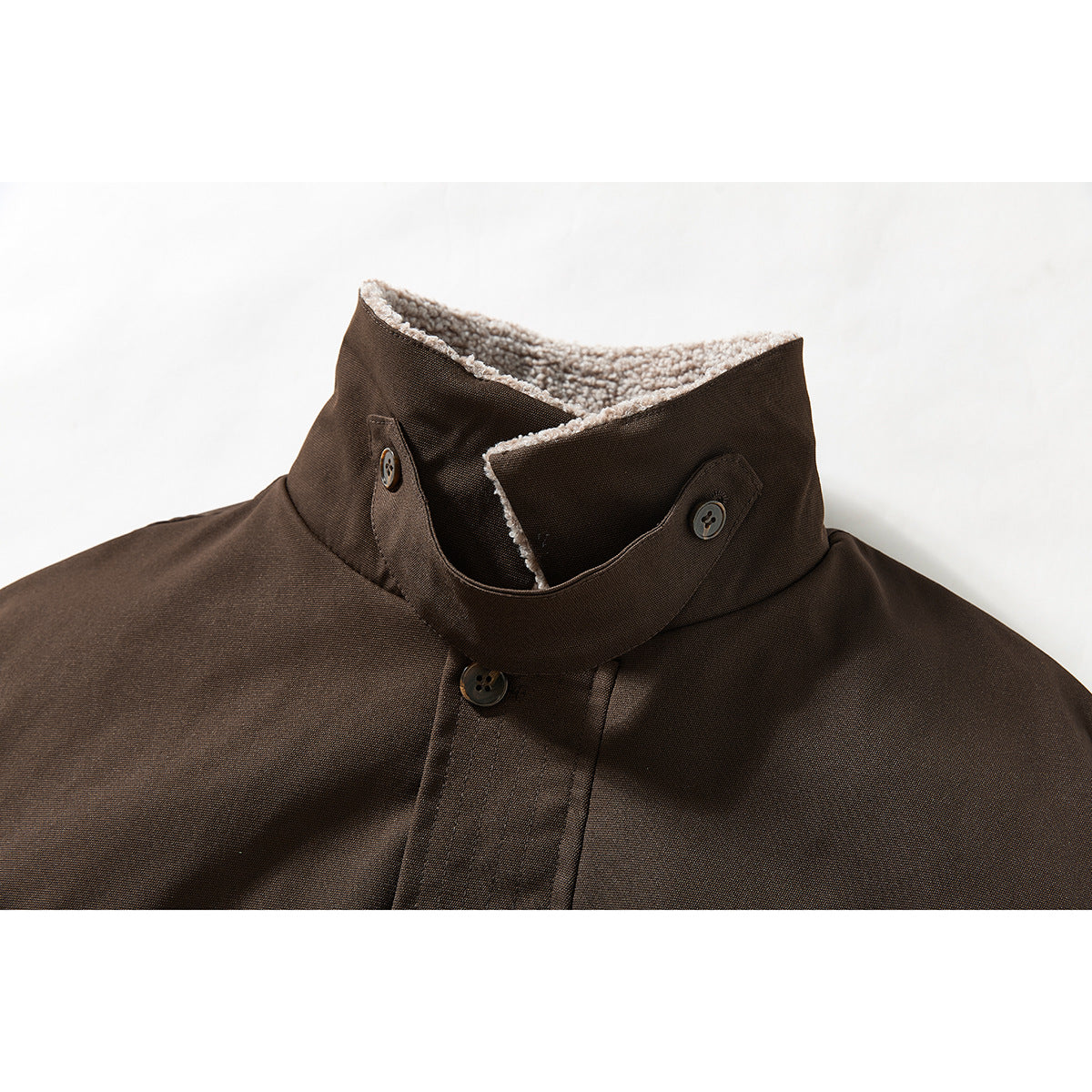 Close-up of a dark brown jacket’s raised collar, showing light sherpa lining and button tabs.