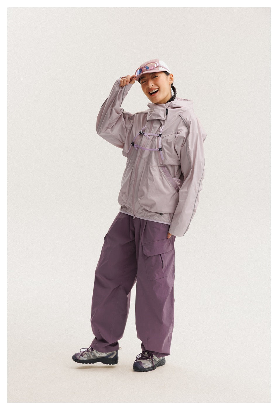 Model wearing a pale lavender hooded jacket with chest straps and loose plum cargo pants.
