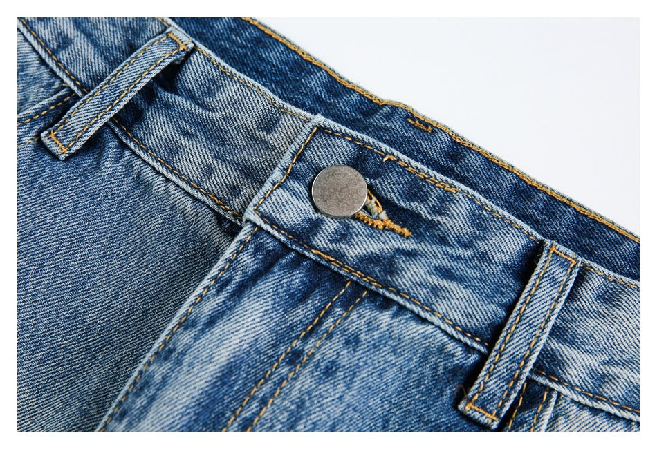 Close-up of blue jeans showing the waistband, metal button, fly seam, and belt loops.