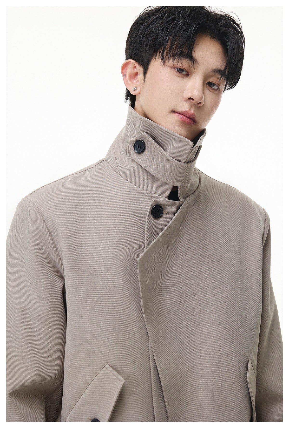 Model wearing a taupe jacket with a high buttoned collar and an asymmetrical front.