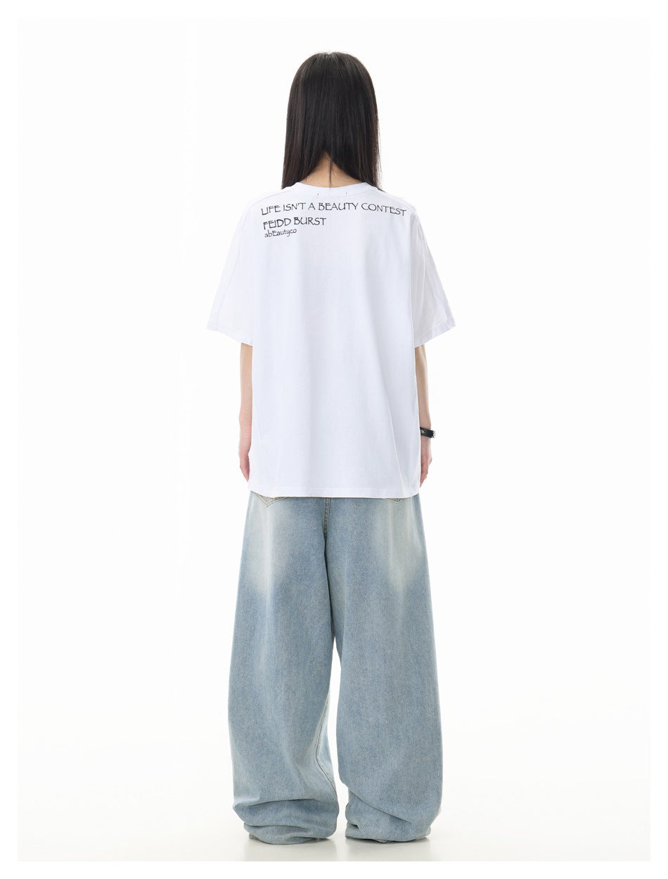 Back view of a model wearing a white oversized T-shirt with small black text across the upper back and wide light-wash jeans.