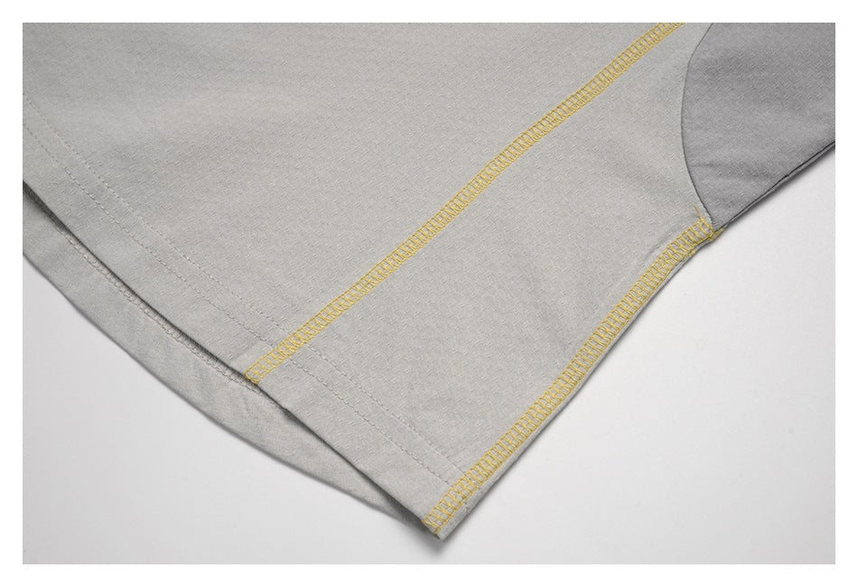 Close-up of a light gray shirt hem with contrasting yellow overlock stitching.