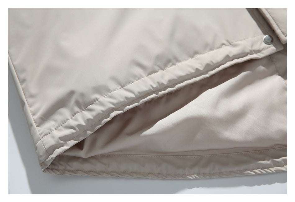 Close-up of a light beige jacket hem with stitched edging and a metal snap.
