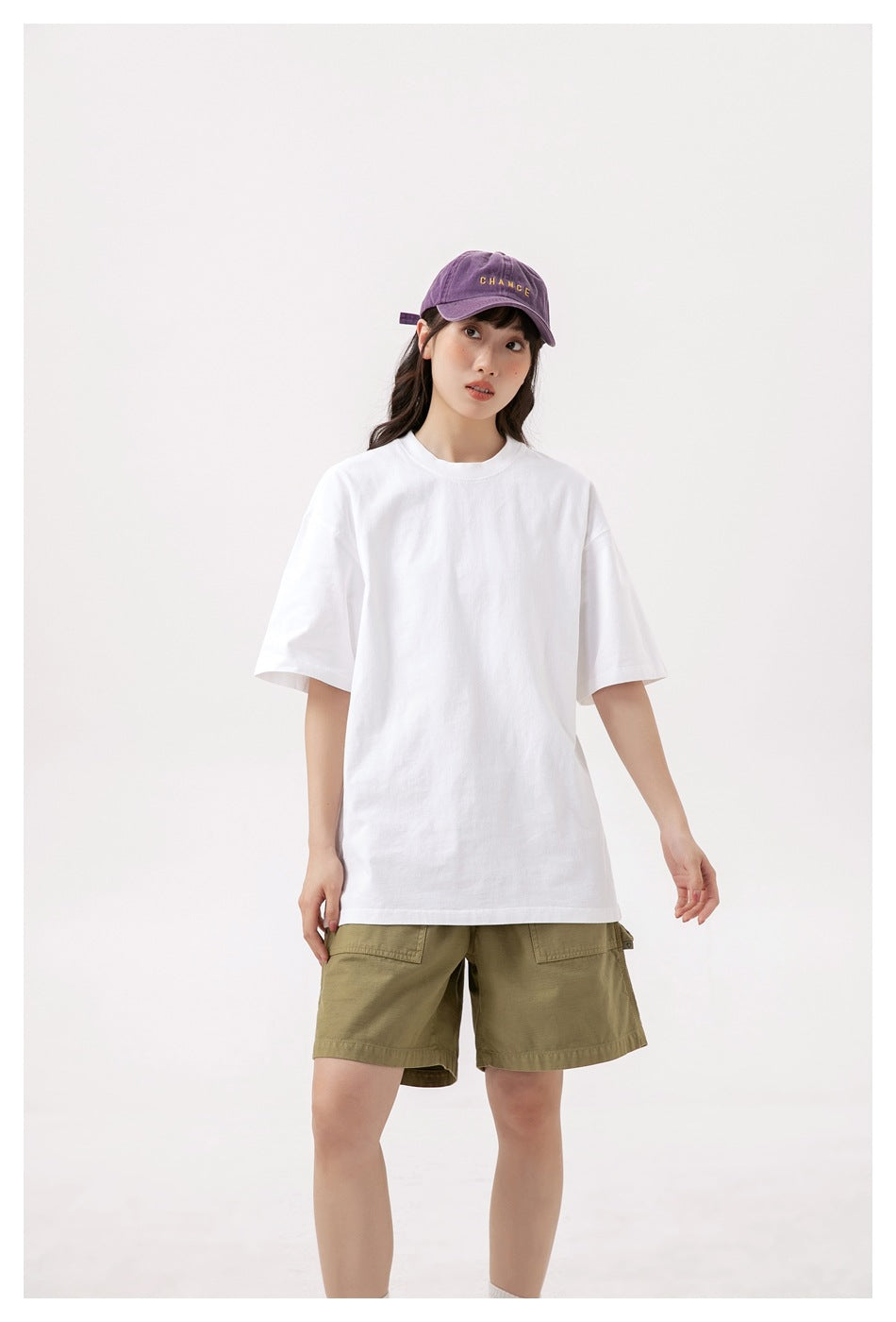Front view of a model in an oversized plain white T-shirt and olive shorts, shown from cap to lower legs.