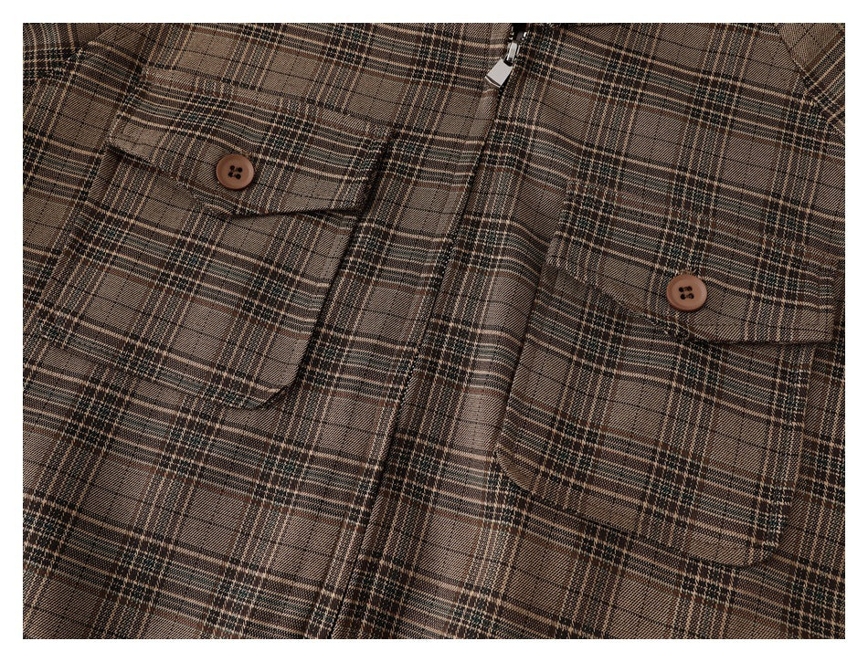 Close-up of a brown plaid jacket front with two button-flap chest pockets and a zipper.