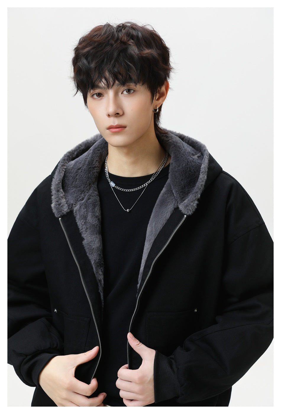 Model wearing a black zip-front hooded jacket with a plush charcoal-gray lining and oversized front pockets.
