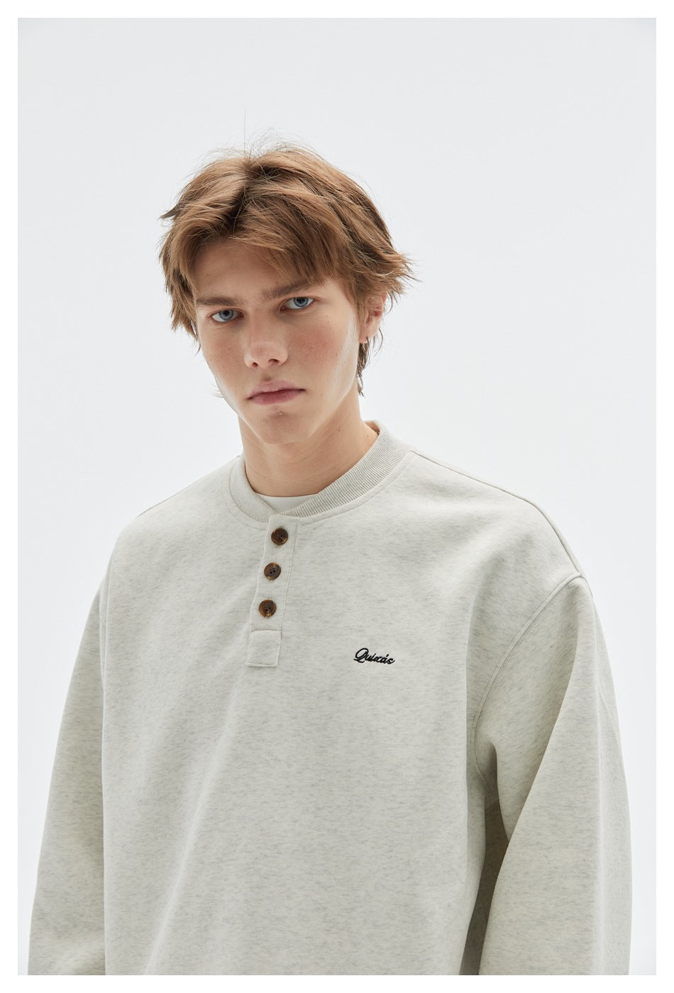 Model wearing an ivory heather sweatshirt with a ribbed collar, three-button placket and small chest embroidery.