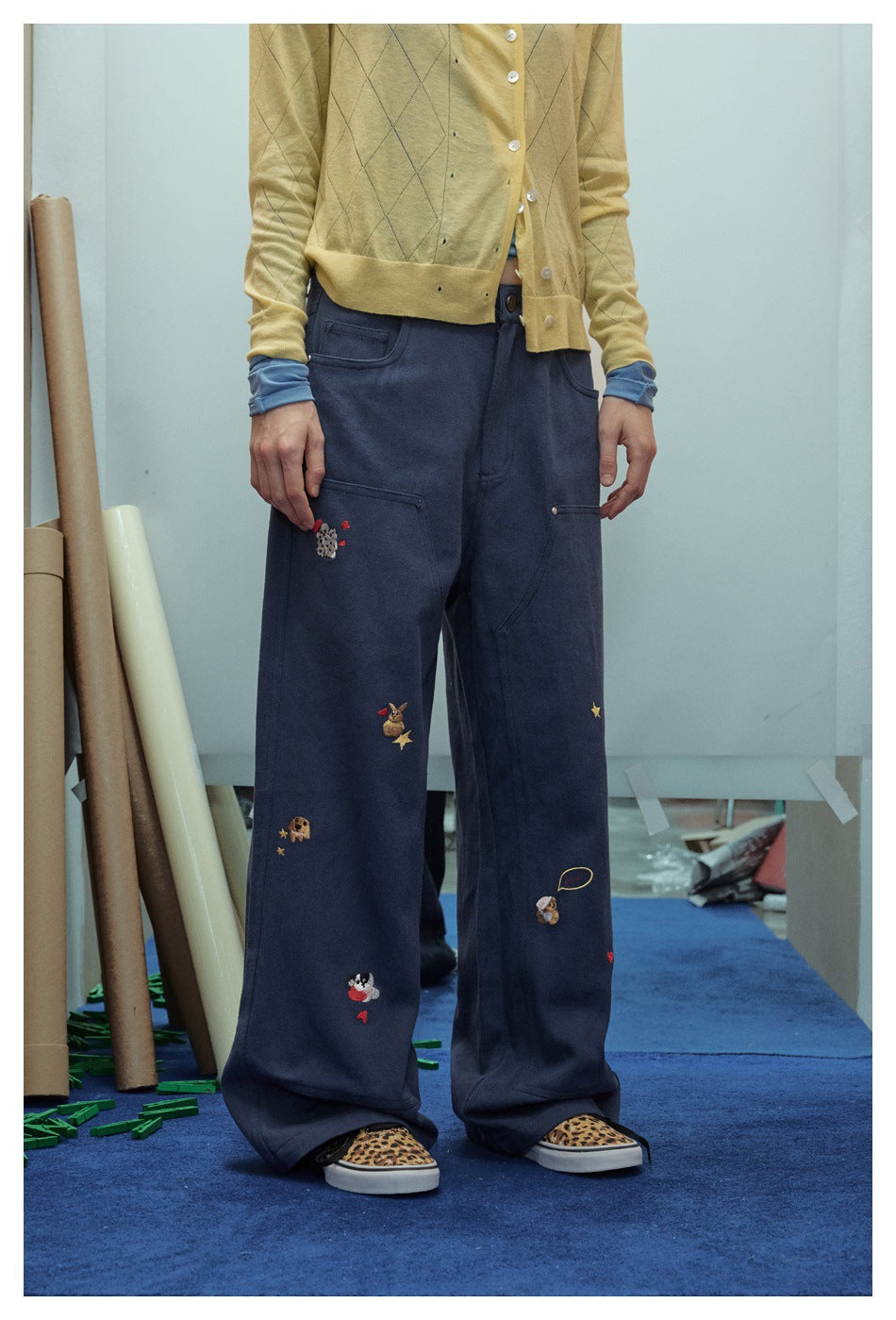 Model wearing navy wide-leg trousers with scattered small embroidered animal, heart, and star motifs.