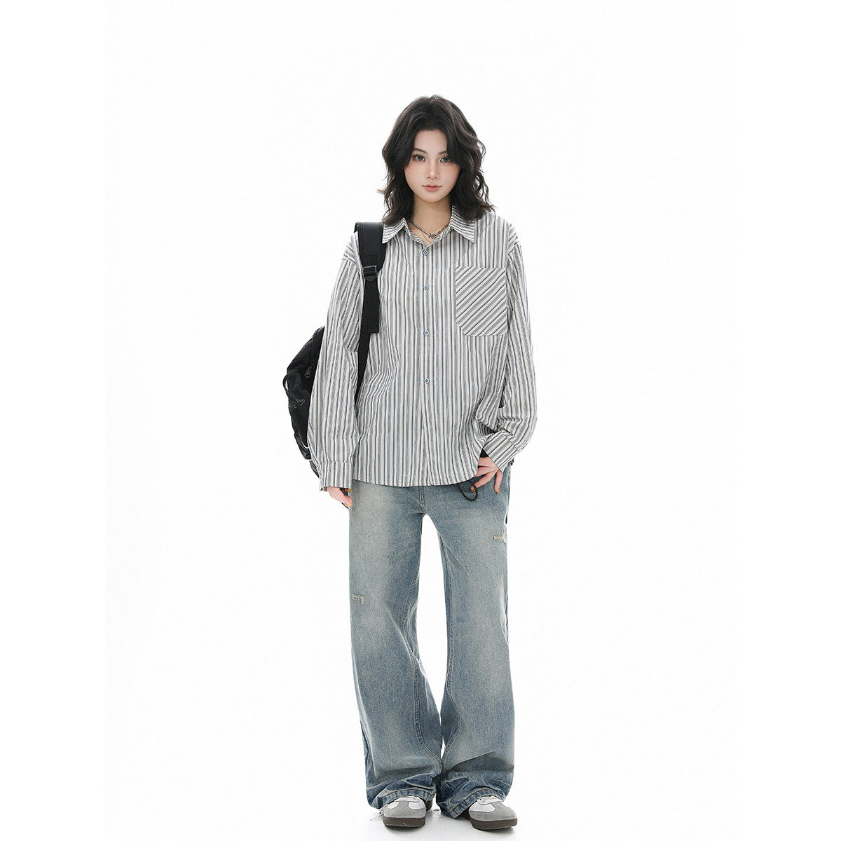 Model wearing an oversized blue-gray striped button-up shirt with a chest pocket and loose light-wash jeans, front view.