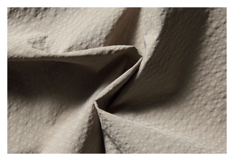 Close-up of beige textured fabric gathered into folds, showing its surface and drape.