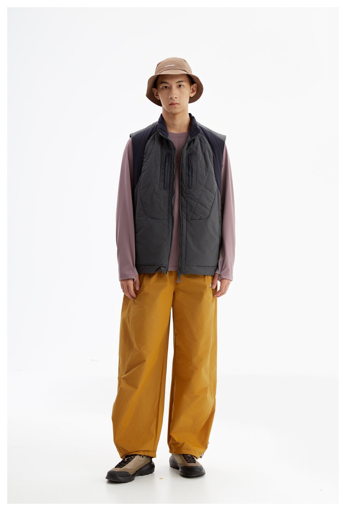 Model wearing a charcoal quilted zip vest with chest pockets over a mauve top, paired with mustard pants.