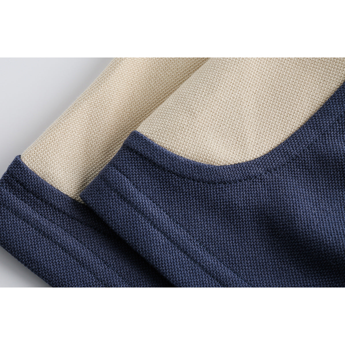 Close-up of cream and navy knit polo fabric, showing the textured weave and curved seam.