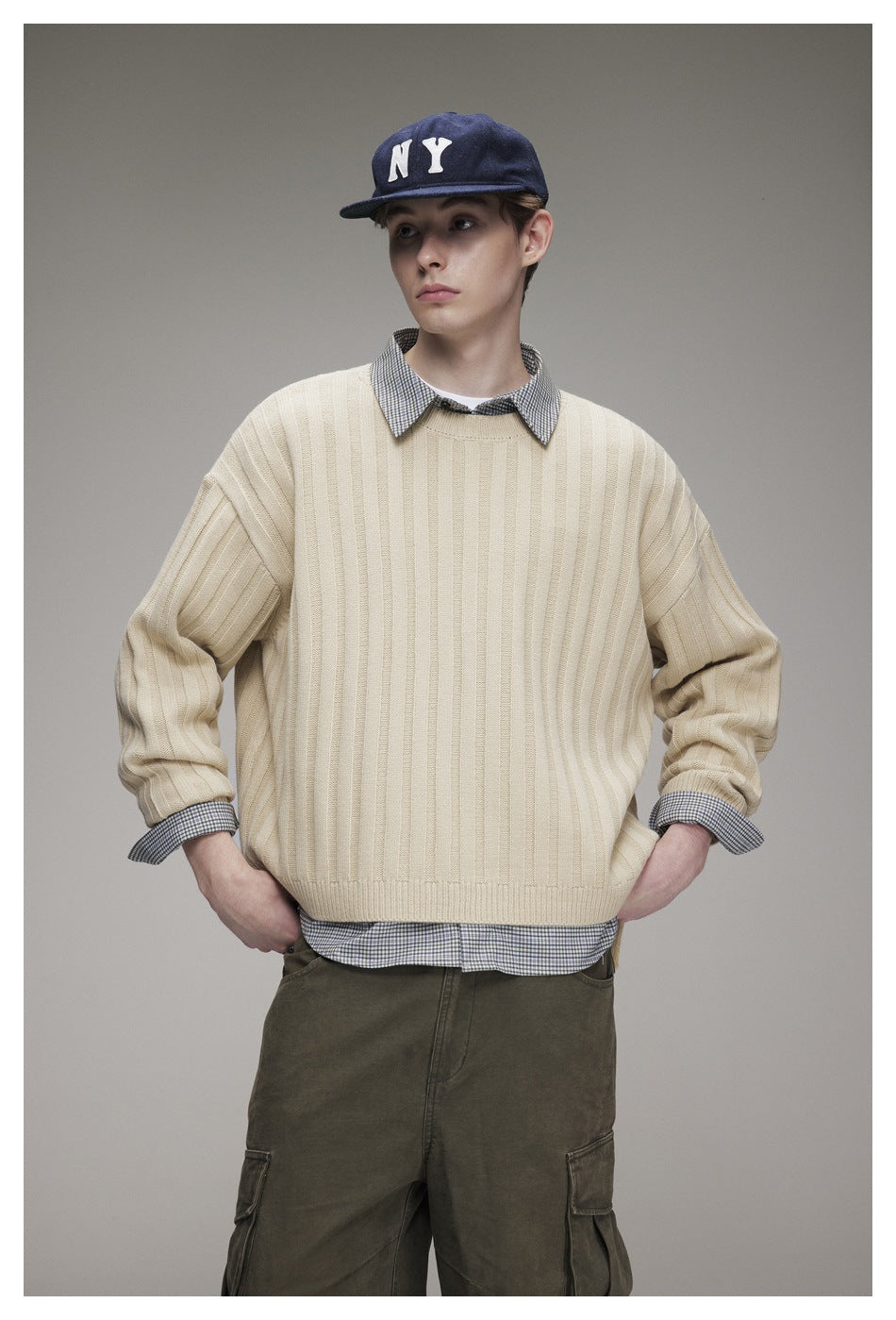 Front view of a model wearing a cream rib-knit sweater over a checked shirt.
