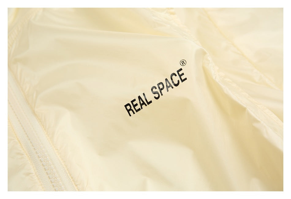 Close-up of a pale cream jacket with black REAL SPACE lettering printed on the fabric.