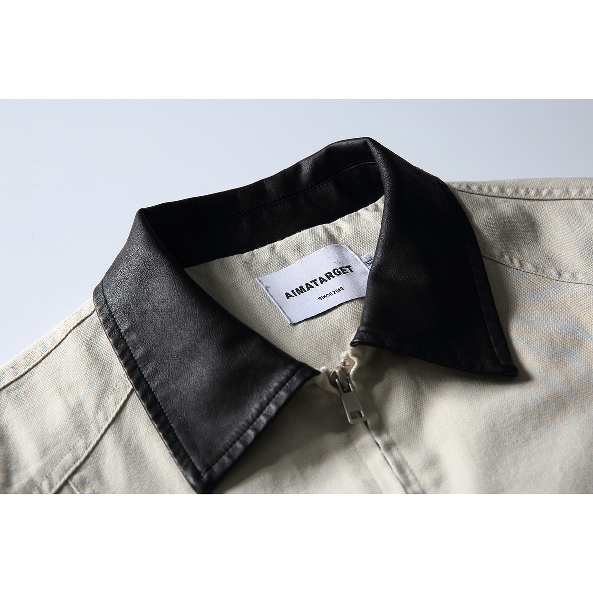 Close-up of an off-white jacket with a black contrast collar, front zipper and sewn neck label.