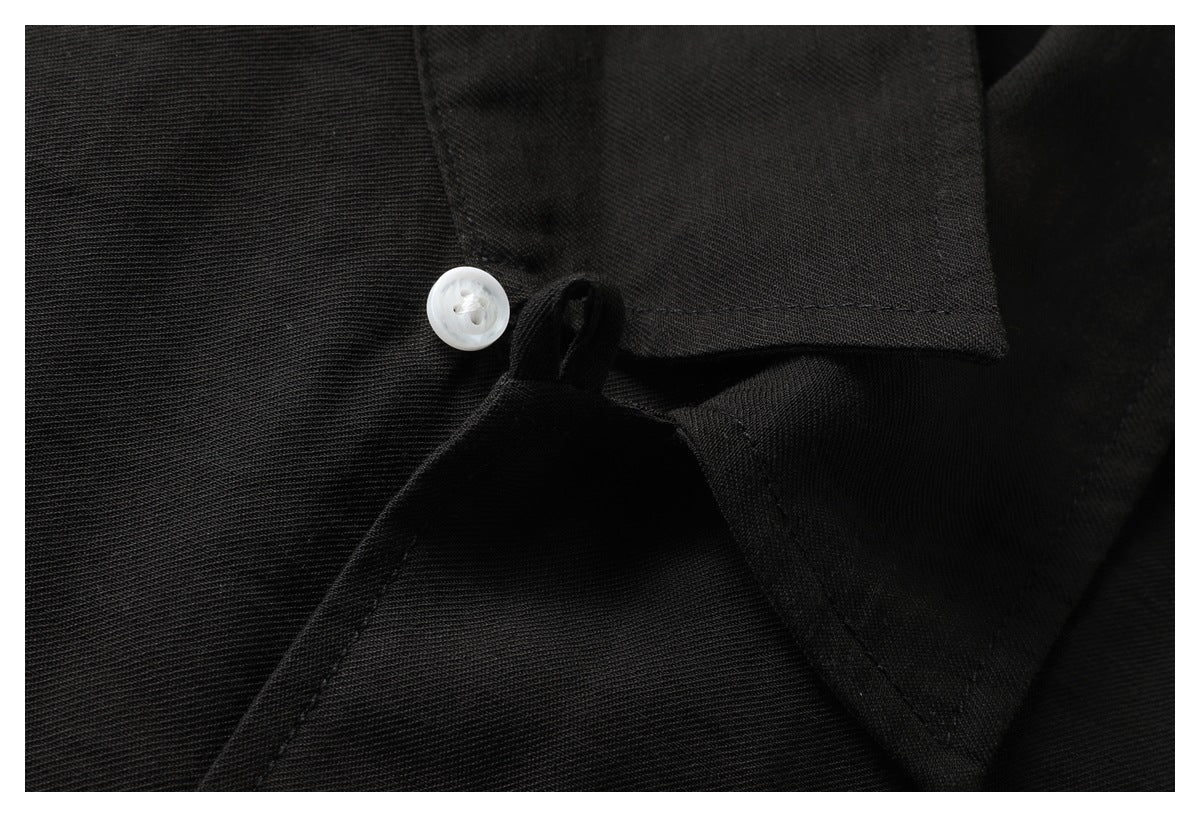Close-up of a white button and stitching at the collar and placket of a black shirt.