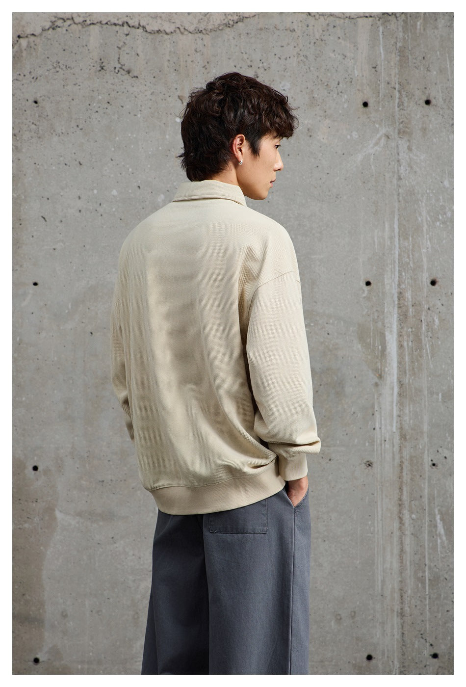Model seen from behind wearing a loose cream collared pullover and dark gray trousers.