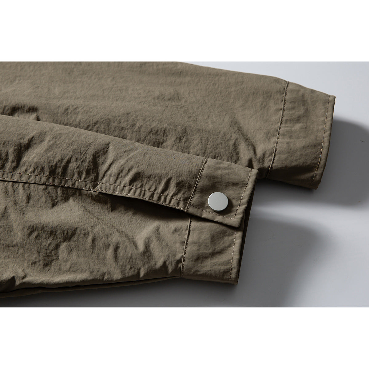 Close-up of the olive-gray jacket's sleeve cuffs, with a light-colored snap button.