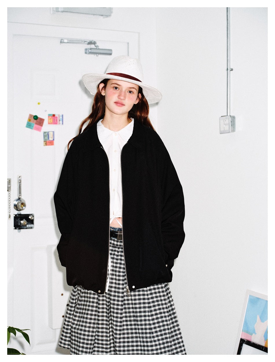 Model wearing an oversized black zip jacket over a white blouse and black-and-white checked skirt, shown from the waist up.