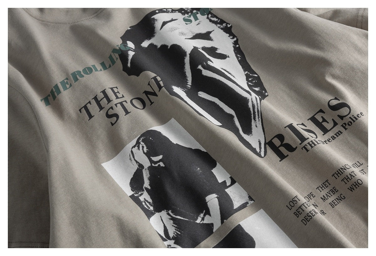 Close-up of a taupe T-shirt with black-and-white rock musician graphics and dark printed lettering.