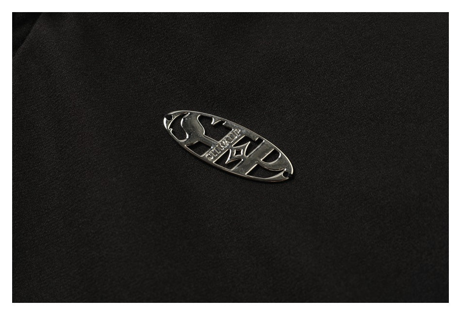 Close-up of a small silver oval emblem attached to black jacket fabric.