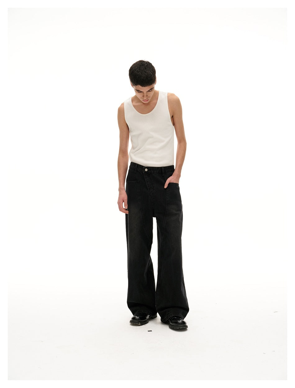 Model looking down with one hand in a pocket, wearing a white tank top and wide black jeans.