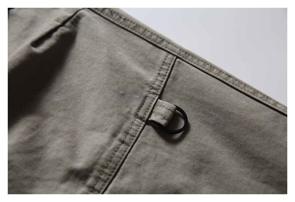 Close-up of gray-olive pants showing a small black D-ring attached beside a seam.