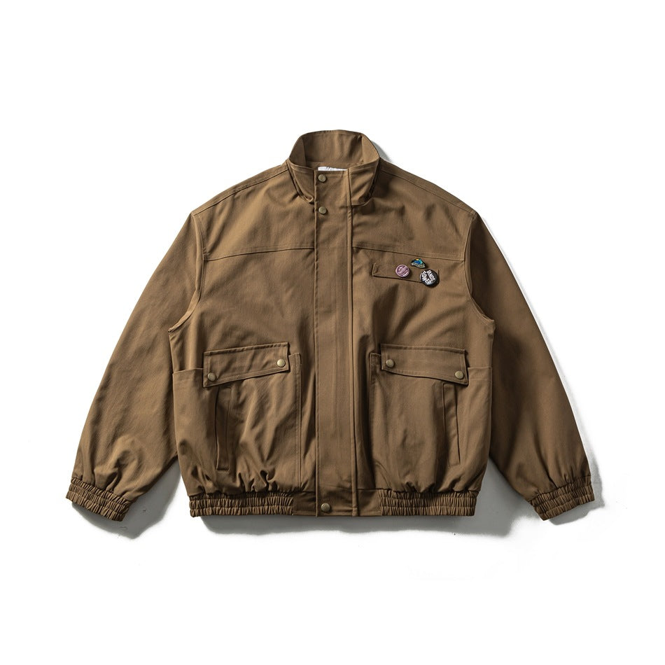 Brown khaki stand-collar jacket flat lay with two flap pockets, chest badges, and elastic cuffs and hem