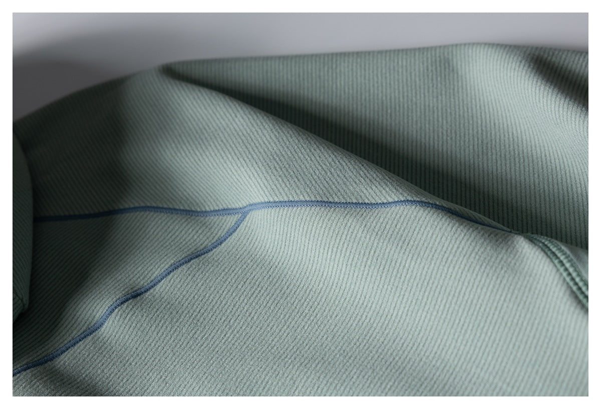 Close-up of sage-gray ribbed fabric with a curved seam finished in blue-gray stitching.