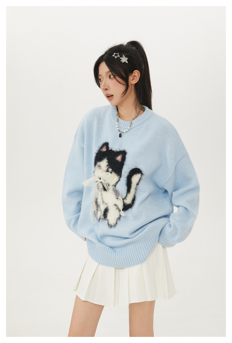 Closer view of a model wearing a light blue sweater with a fluffy black-and-white cat applique and bow.