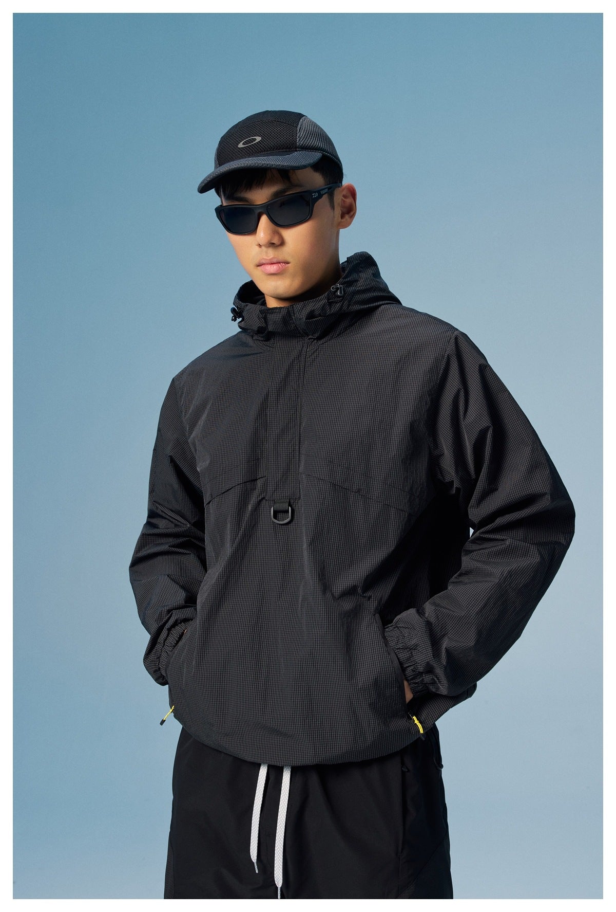 Front view of a man wearing a black hooded windbreaker with subtle grid texture and black pants.