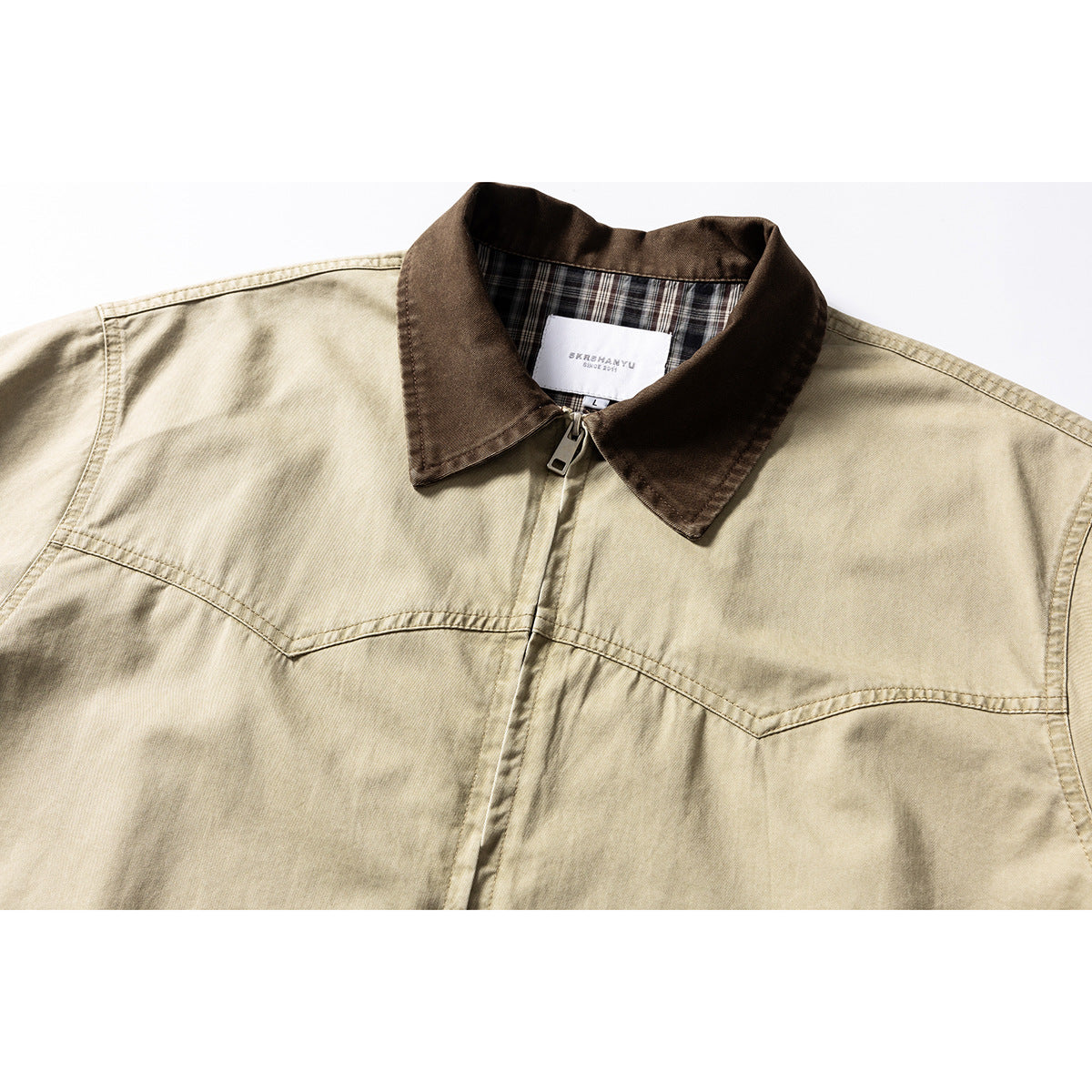 Close-up of a beige zip-front shirt jacket with a dark brown collar and plaid inner collar lining.